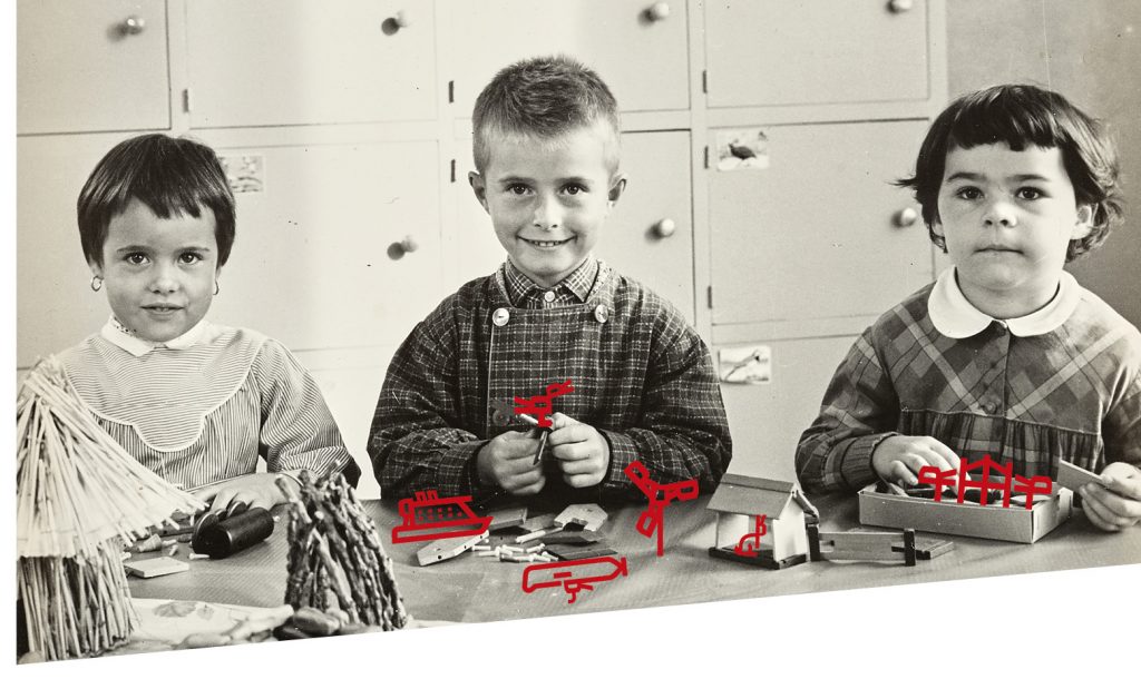 Photographie en noir et blanc de trois jeunes élèves attablés en train de participer à des jeux de construction.