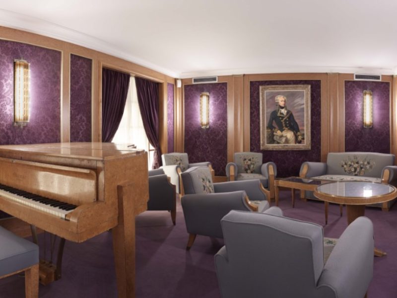 Reconstitution du salon de musique du paquebot Liberté à Escal'Atlantic avec ses meubles et son piano et une tapisserie violette.