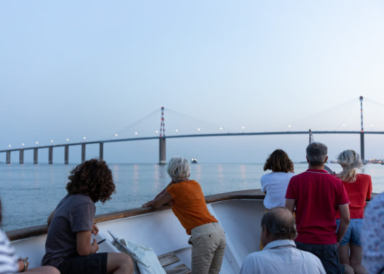 Passagers appuyés sur le pont du bateau de croisière et regardant le pont de Saint-Nazaire à la nuit tombée.