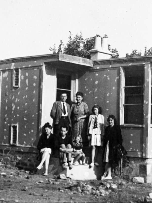 Photographie en noir et blanc d'une famille posant devant un bungalow inachevé,pendant la reconstruction de Saint-Nazaire.