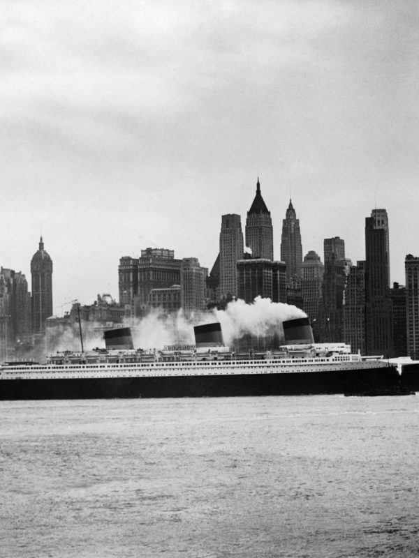 Photographie en noir et blanc représentant le paquebot Normandie devant les immeubles à New York.