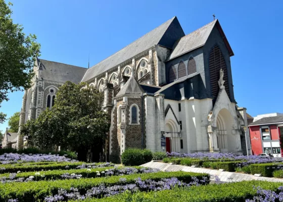 Photographie de la façade de l'église Saint-Nazaire avec au premier plan des parterres d'agapanthes en fleurs.