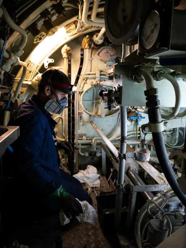 Un membre de l'équipe du chantier de restauration équipé d'un masque nettoie l'intérieur du sous-marin Espadon.
