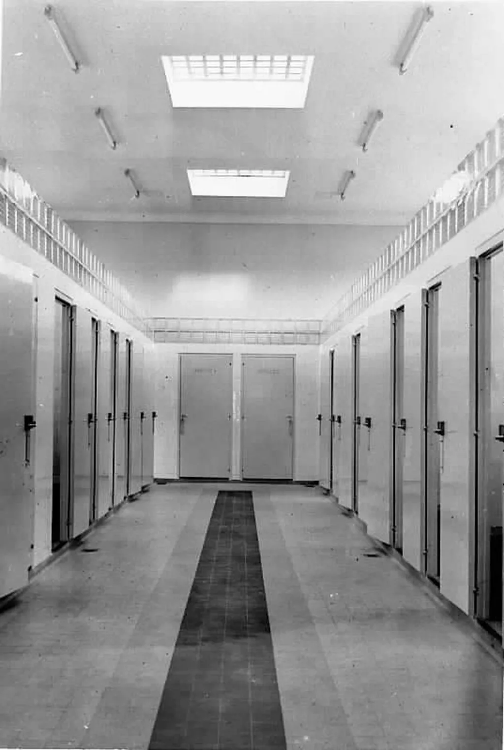 Photographie en noir et blanc d'un couloir avec de chaque côtés des portes à l'intérieur des bains douches de Saint-Nazaire.