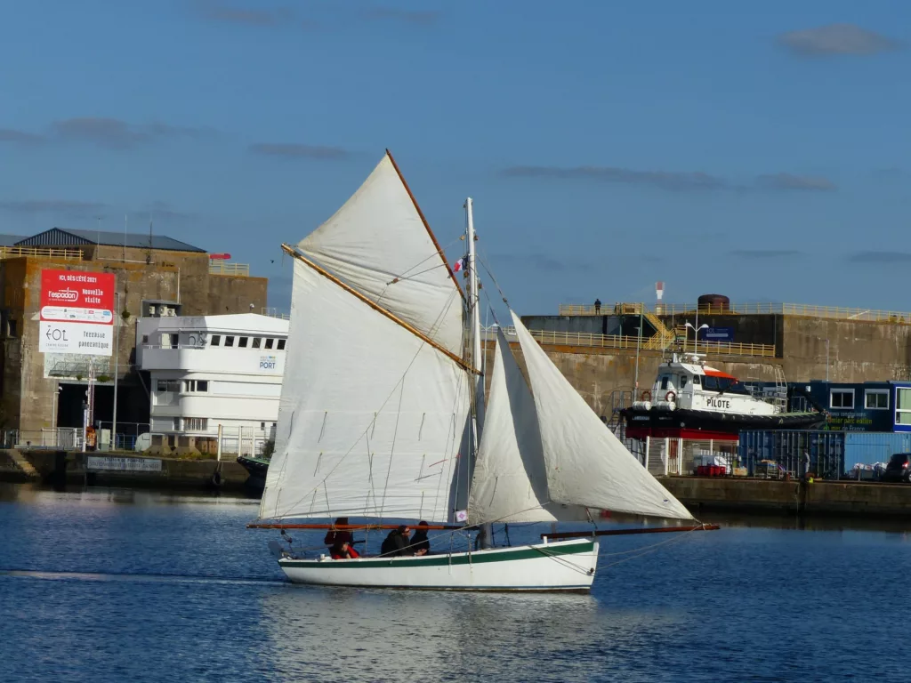 Voilier à coque et voiles blanches navigant dans le bassin de Saint-Nazaire